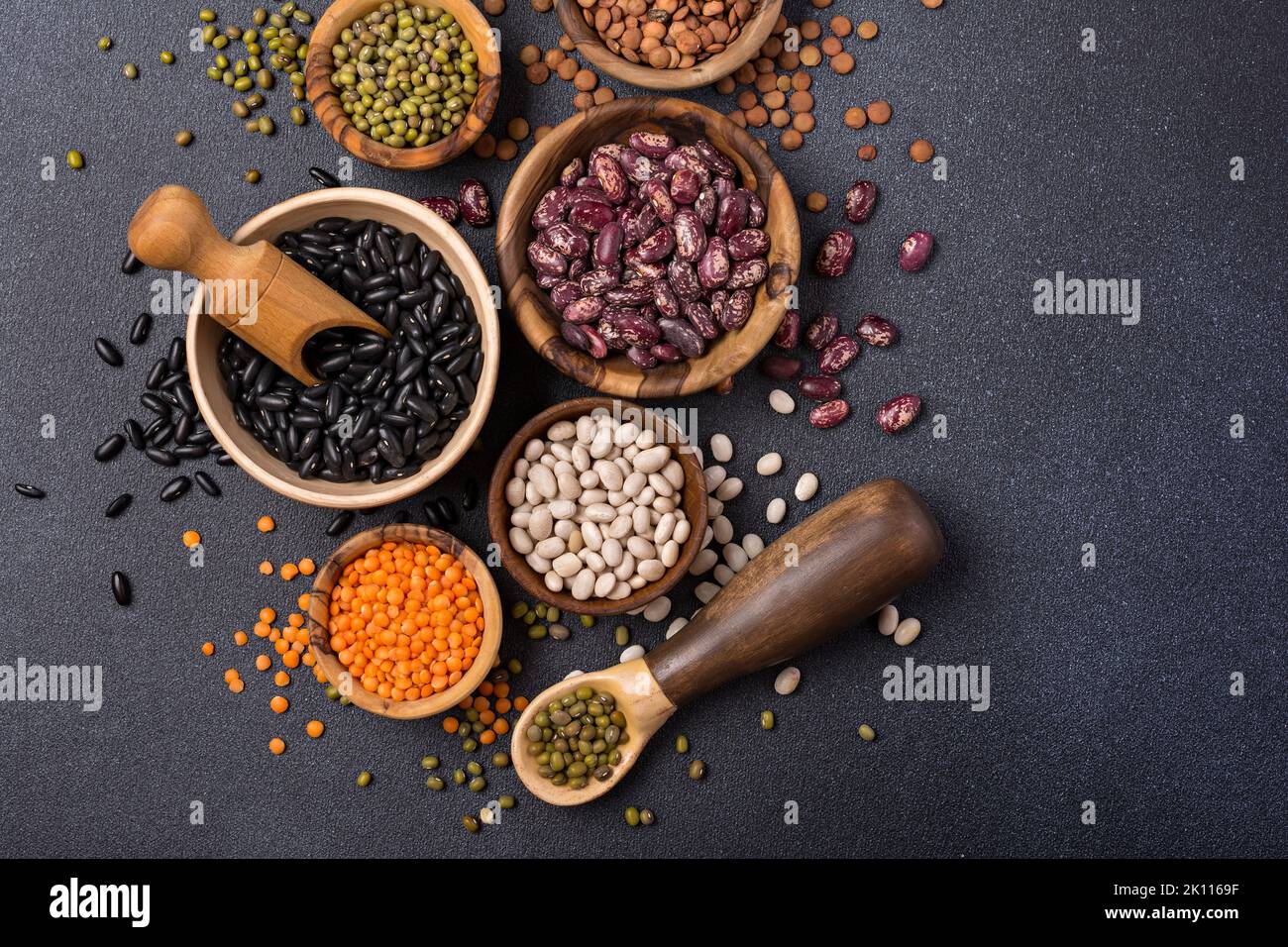 Top view of different beans, lentils, mung or maash in bowls on dark concrete background Stock Photo