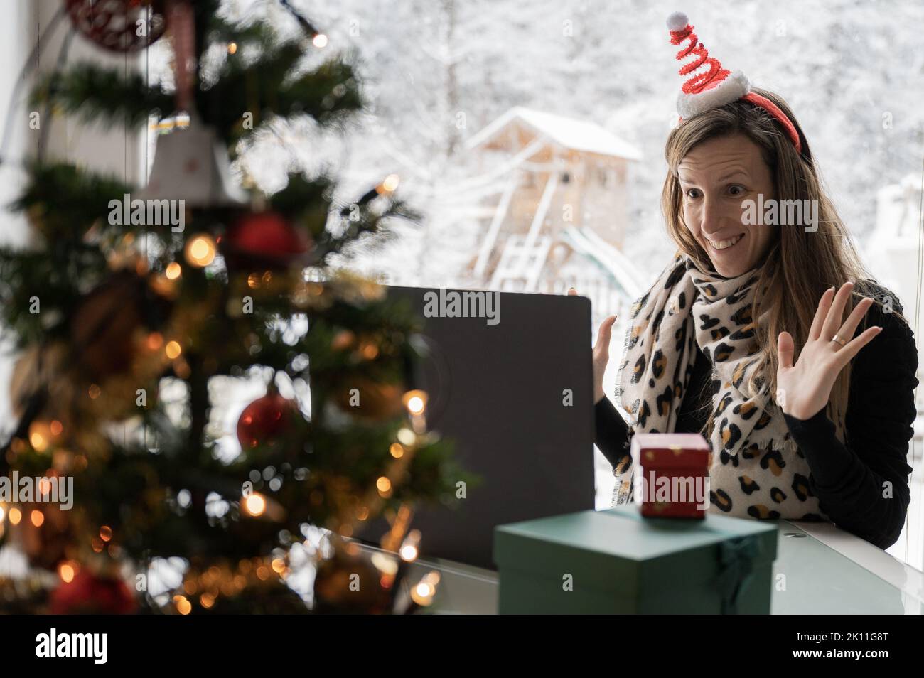 Cheerful young woman with christmas holiday hat on her head excitedly wawing to a laptop computer as she meets her family or friends via online video Stock Photo