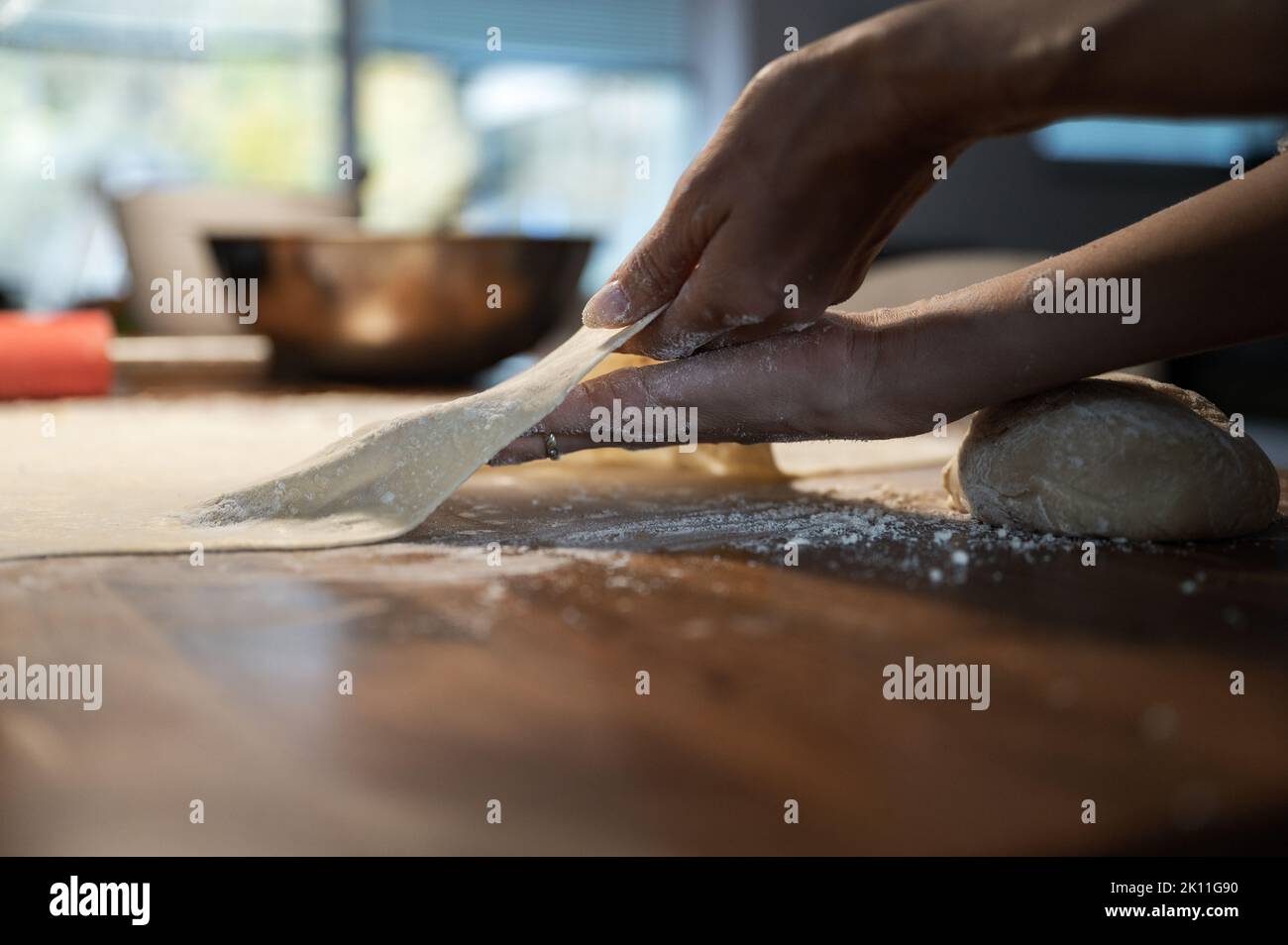 Low angle view of a woman stretching and pulling homemade vegan pastry dough on a domestic flour dusted dining table. Stock Photo