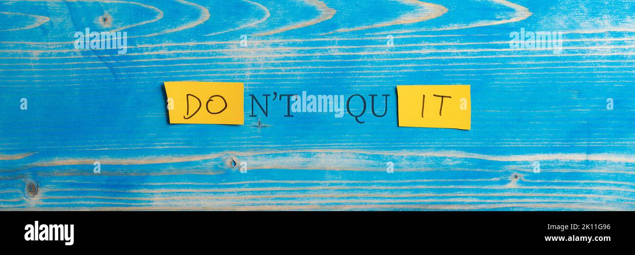 Wide view image of a Dont quit, Do it sign spelled on yellow papers placed on aged blue wooden board. Stock Photo
