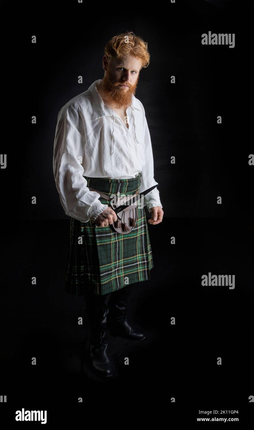 A Scottish man with red hair and beard wearing a kilt  and holding a weapon Stock Photo