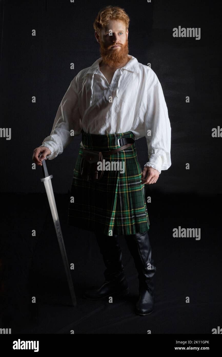 A Scottish man with red hair and beard wearing a kilt  and holding a weapon Stock Photo