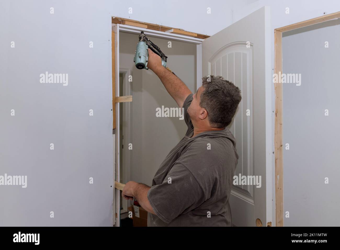 A trim carpenter installs interior doors in a newly constructed house as part of the construction process Stock Photo