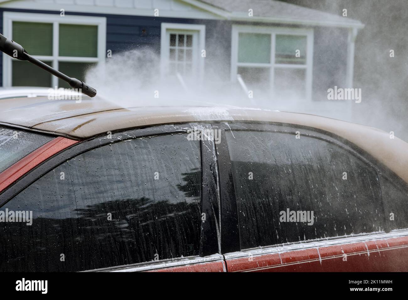 A man is washing a car under a high pressure jet spraying water with a cleaning agent Stock Photo