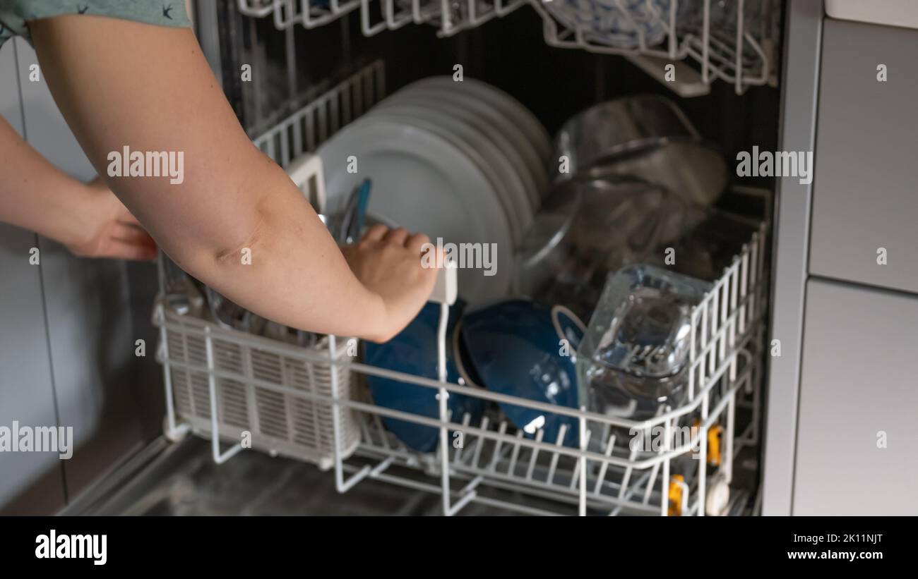 hands sort clean dishes from the dishwasher. Plates, forks and glasses in the dishwasher.Dishwasher with clean dishes.Appliances for the kitchen. Stock Photo