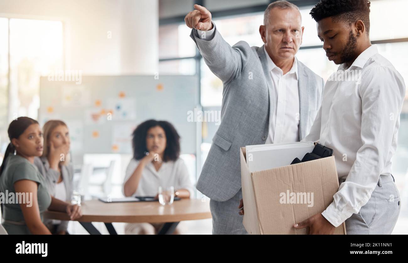 Black man, sad and fired by boss in a meeting holding a box in disappointment at the office. Manager or company leader pointing to the exit and firing Stock Photo