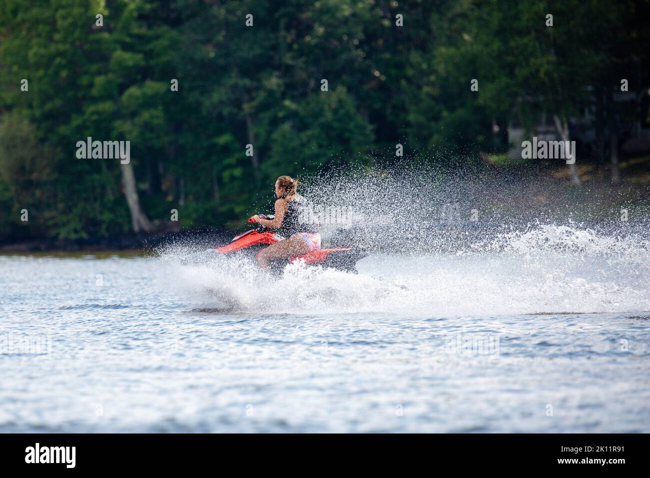 Lake Nokomis, Tomahawk, Wisconsin, USA, August, 20, 2022 - Girl on a jet ski flying across the lake, horizontal Stock Photo