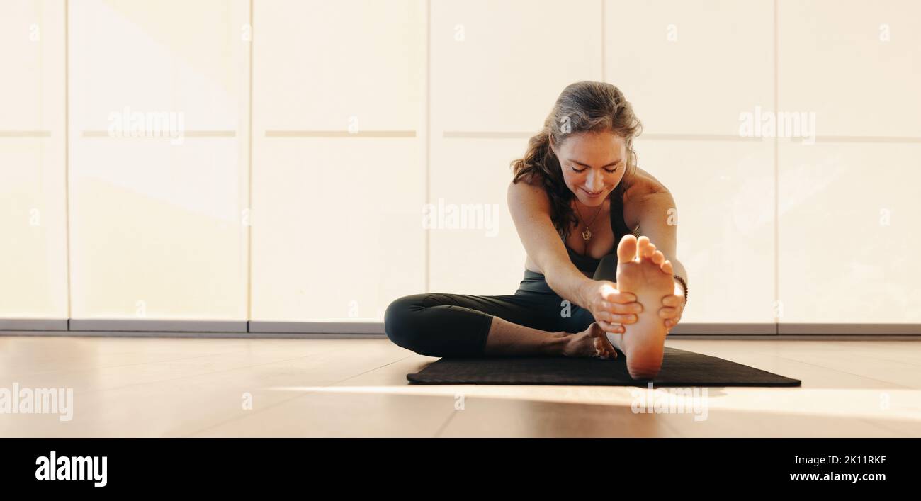 Elderly woman doing a head to knee pose on an exercise mat. Mature woman doing a stretching exercise during a yoga session. Senior woman practicing a Stock Photo