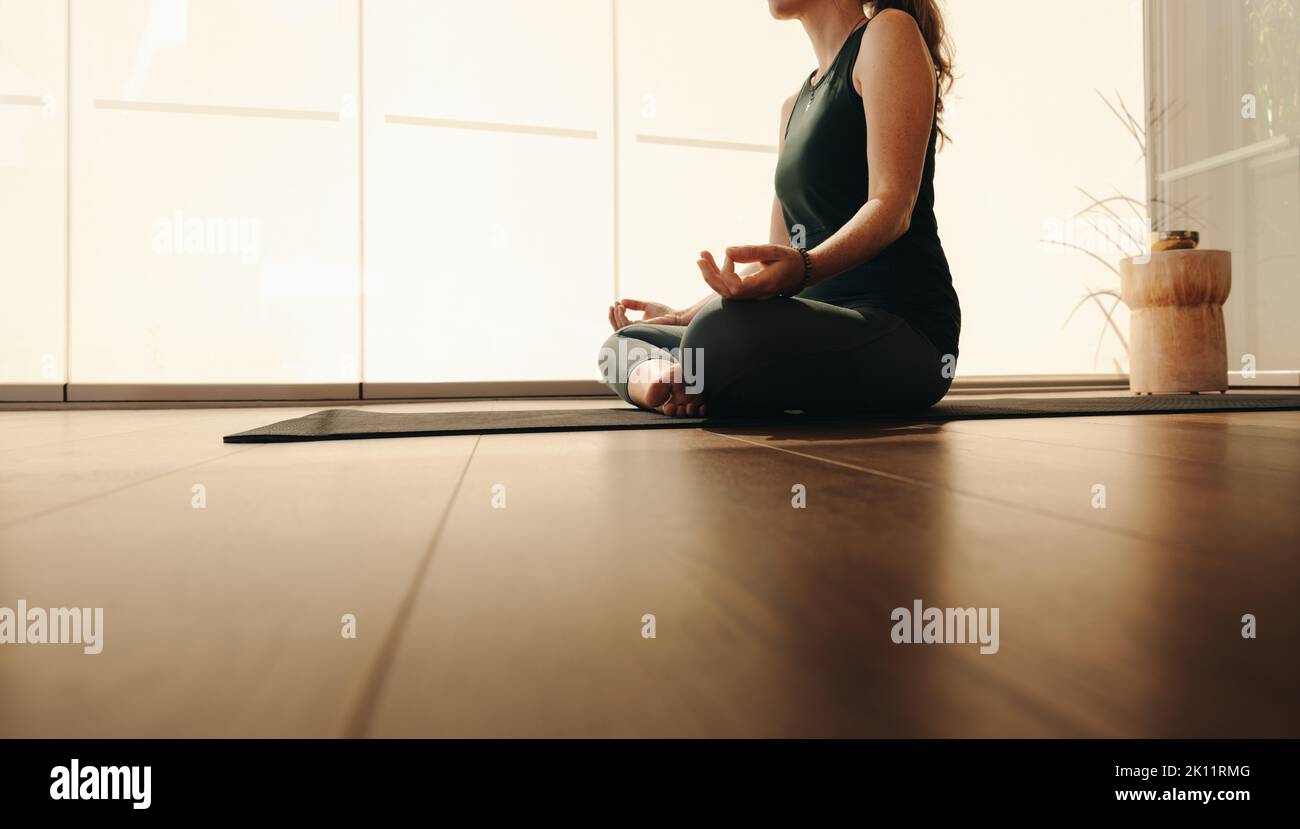 Unrecognisable woman meditating during a session of hatha yoga. Mature woman doing a breathing exercise while sitting in easy pose. Senior woman pract Stock Photo
