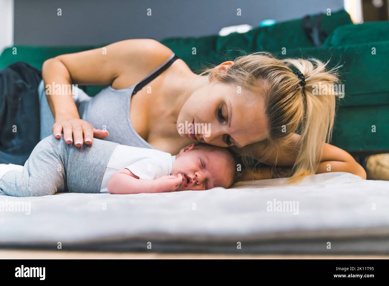 Adorable newborn baby boy with cute brown hair, sleeping peacefully on his stomach on a bed at home with his young caucasian mom laying with him, gently touching and hugging her son. High quality photo Stock Photo