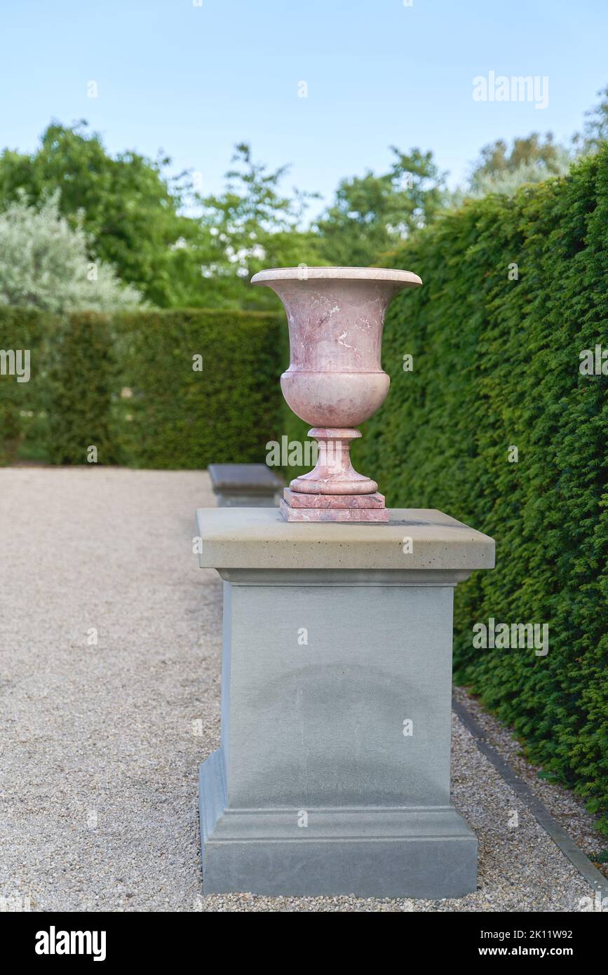 Vase on a pedestal as a decoration on a path in a very well-kept garden Stock Photo