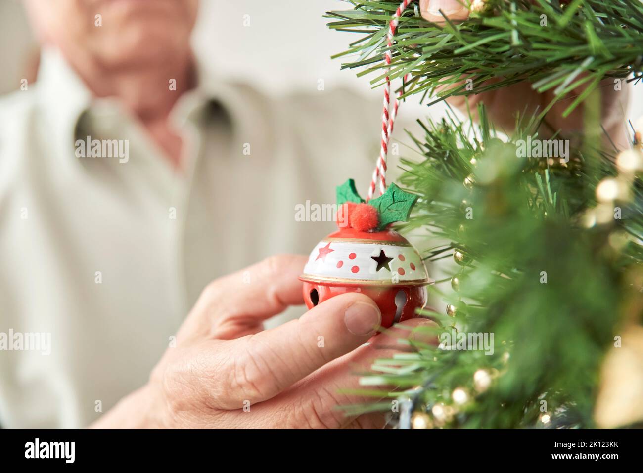 Unrecognizable senior man decorating a Christmas tree at home, male hands hanging a ball on a branch. Stock Photo