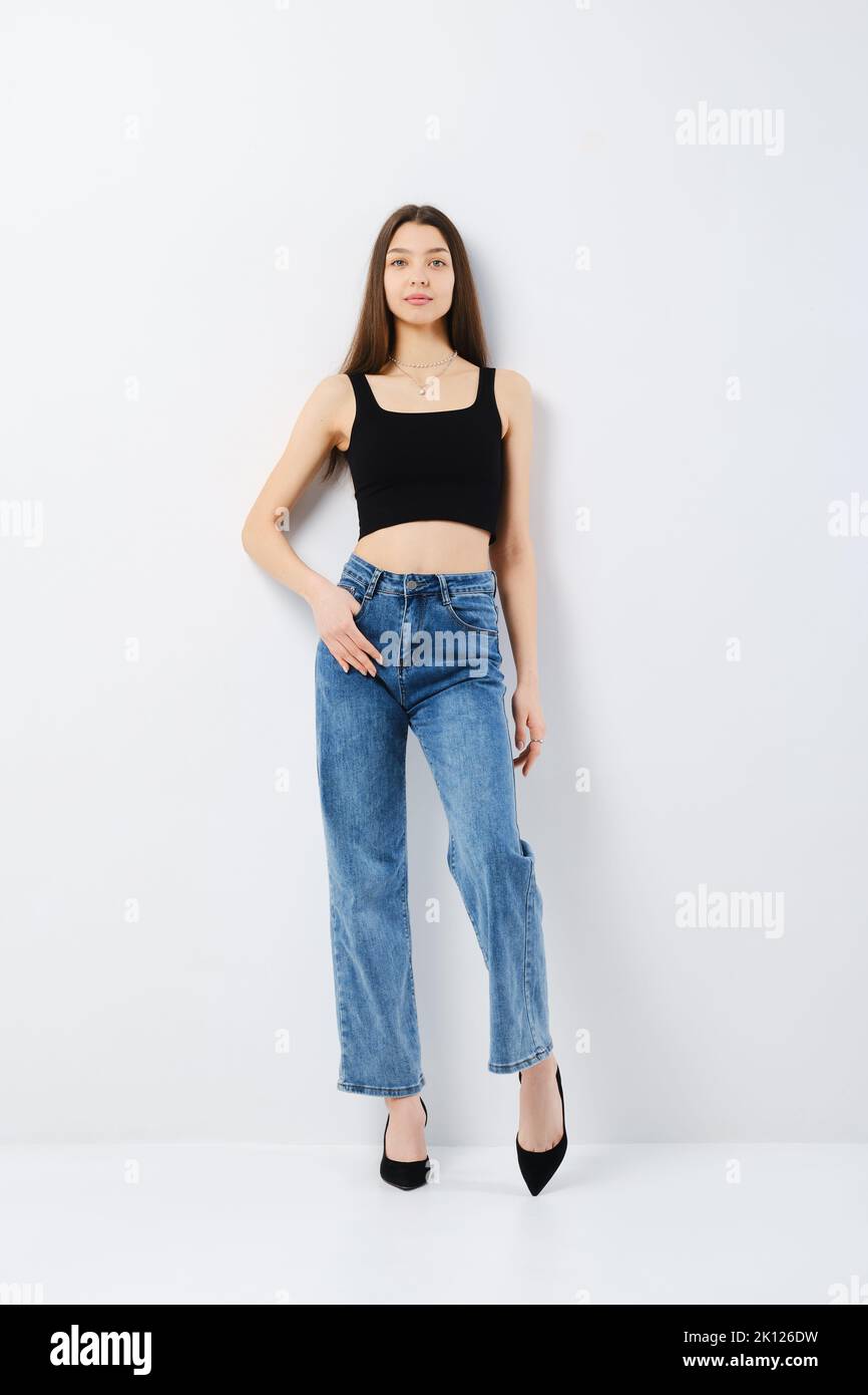 Full length portrait of young woman in black tank top and wide jeans ...