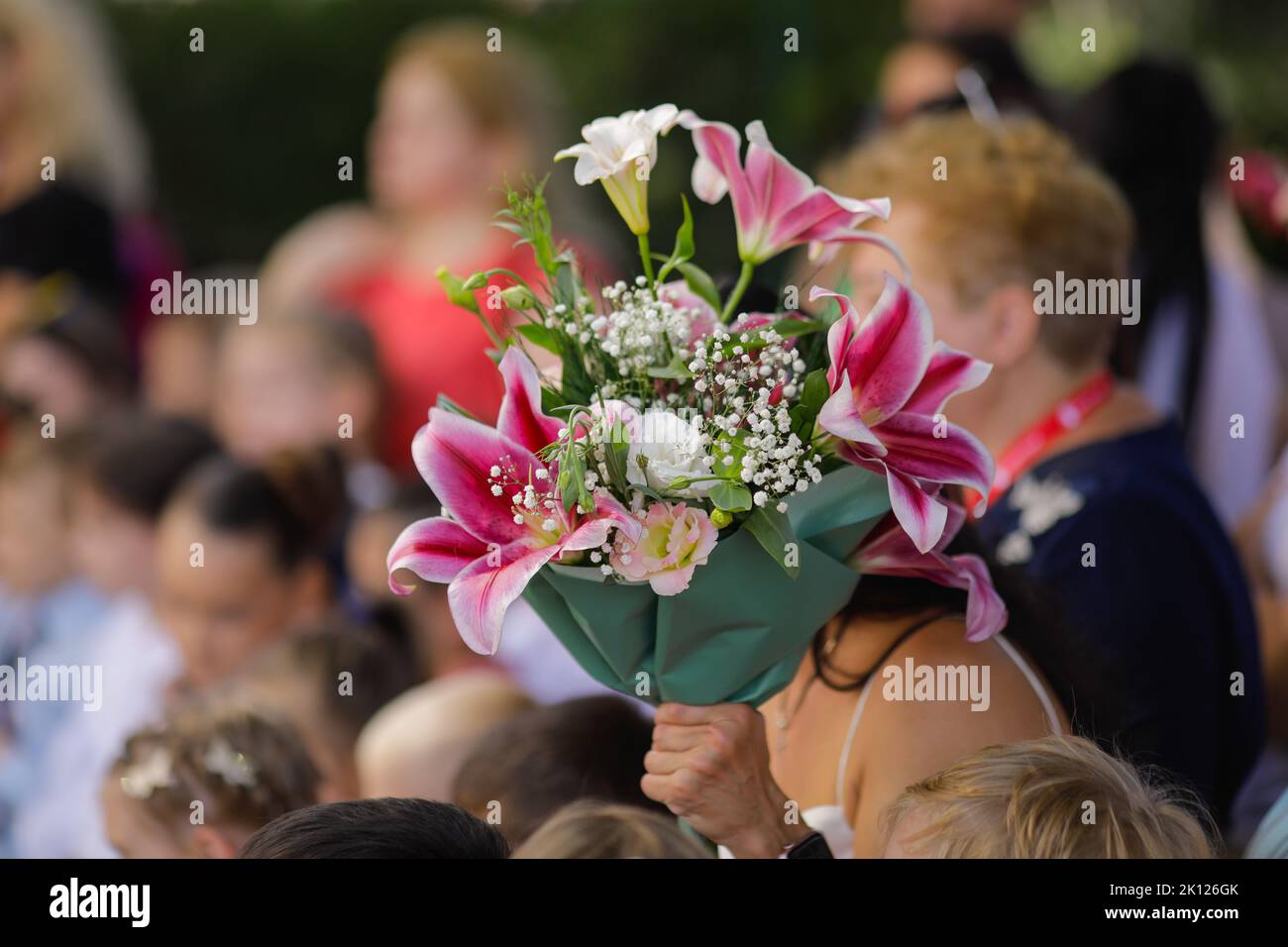 Shallow depth of field (selective focus) details with a woman holding flowers during the first day of school for her child. Stock Photo