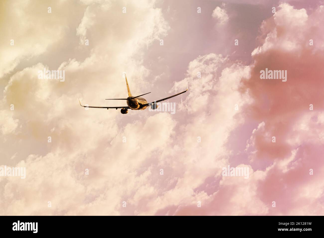 Silhouette of an airplane taking off high into the sky at sunset with a warm shade of clouds Stock Photo