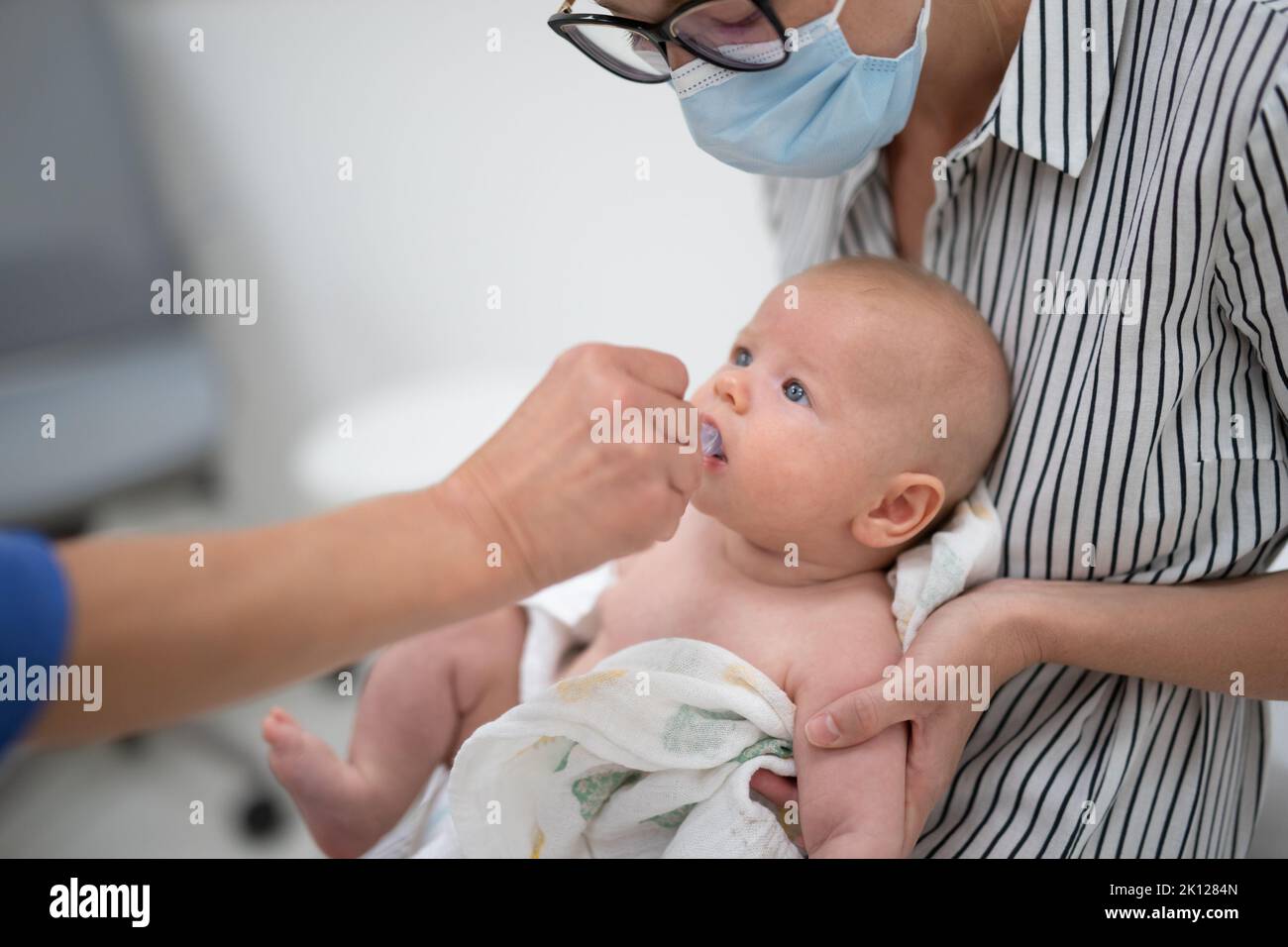 Pediatrician administring oral vaccination against rotavirus infection to little baby in presence of his mother. Children health care and disease Stock Photo