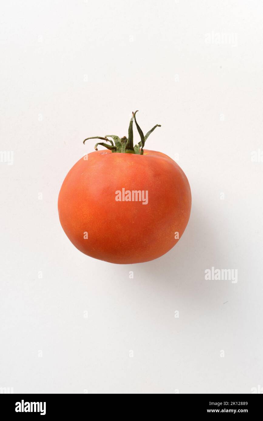 Detail of whole tomato with leaves isolated on white table. Vertical composition. Stock Photo