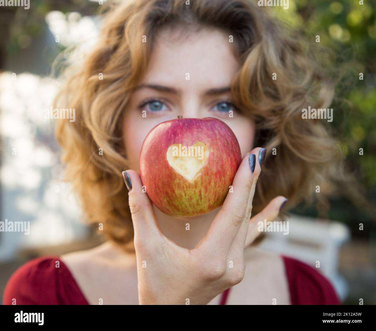 healthy eating - young woman holds a red apple in front of her face with a heart cut out in it. selective focus. proper vitamin nutrition. love concep Stock Photo