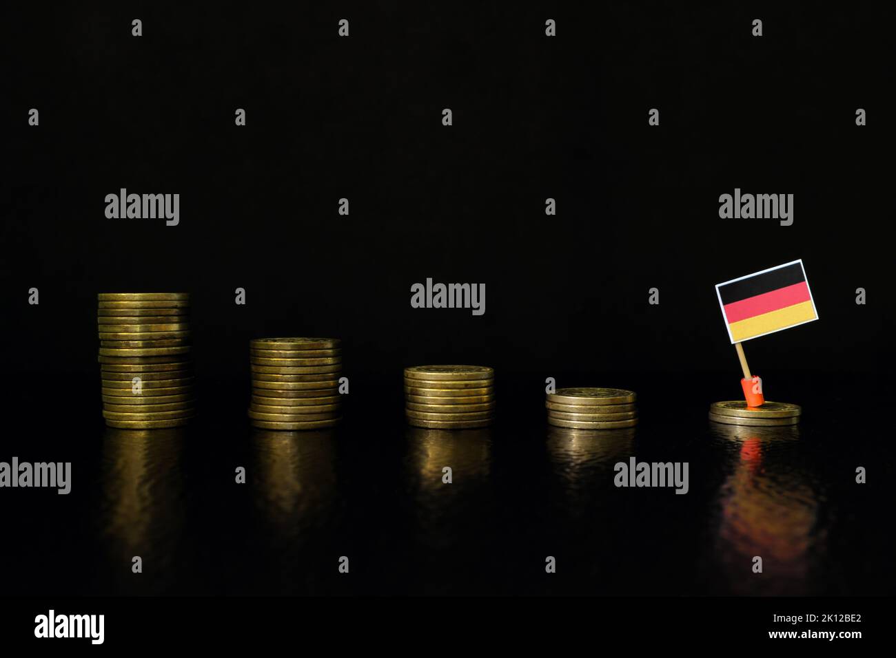 Germany economic recession, financial crisis and currency depreciation concept. German flag in decreasing stack of coins in dark black background. Stock Photo
