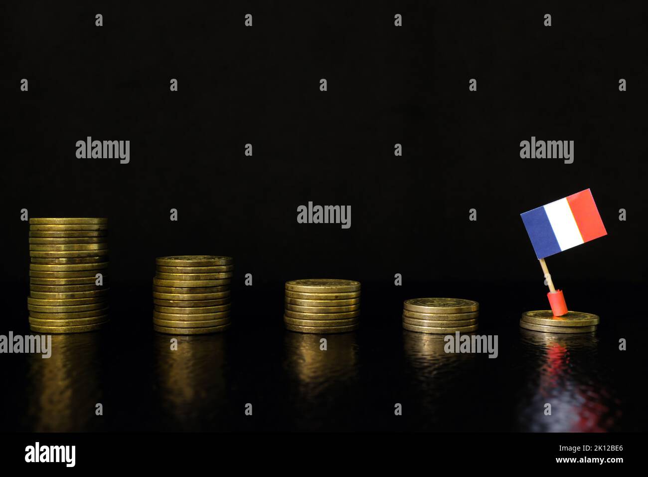France economic recession, financial crisis and currency depreciation concept. French flag in decreasing stack of coins in dark black background. Stock Photo