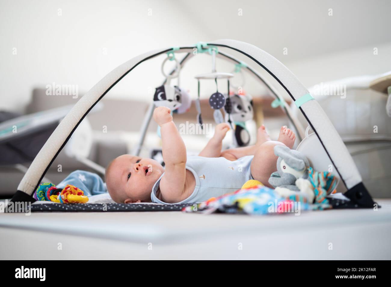 Cute baby boy playing with hanging toys arch on mat at home Baby activity and play center for early infant development. Baby playing at home Stock Photo