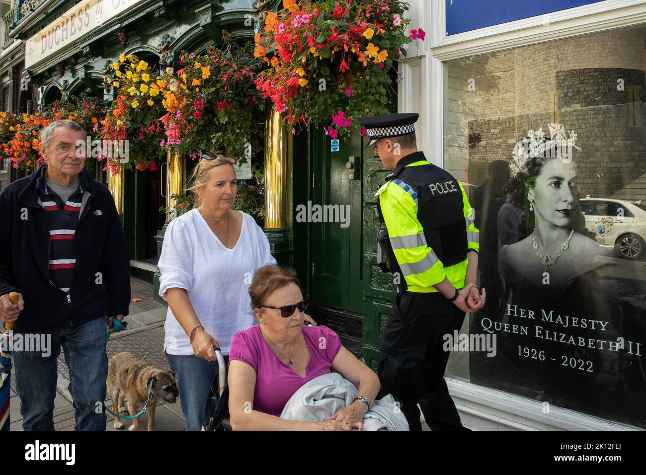 Windsor, UK. 14th September, 2022. A police officer and members of the public pass a tribute to Queen Elizabeth II displayed in a shop window. Queen Elizabeth II, the UK's longest-serving monarch, died at Balmoral aged 96 on 8th September after a reign lasting 70 years and will be buried in the King George VI memorial chapel in Windsor following a state funeral in Westminster Abbey on 19th September. Credit: Mark Kerrison/Alamy Live News Stock Photo