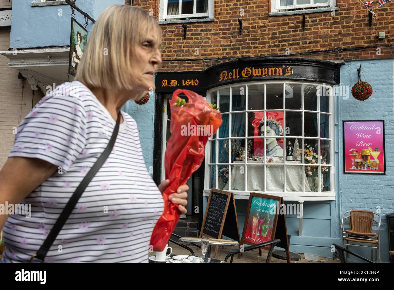 Windsor, UK. 14th September, 2022. A woman carrying flowers passes a tribute to Queen Elizabeth II displayed in a restaurant window. Queen Elizabeth II, the UK's longest-serving monarch, died at Balmoral aged 96 on 8th September after a reign lasting 70 years and will be buried in the King George VI memorial chapel in Windsor following a state funeral in Westminster Abbey on 19th September. Credit: Mark Kerrison/Alamy Live News Stock Photo