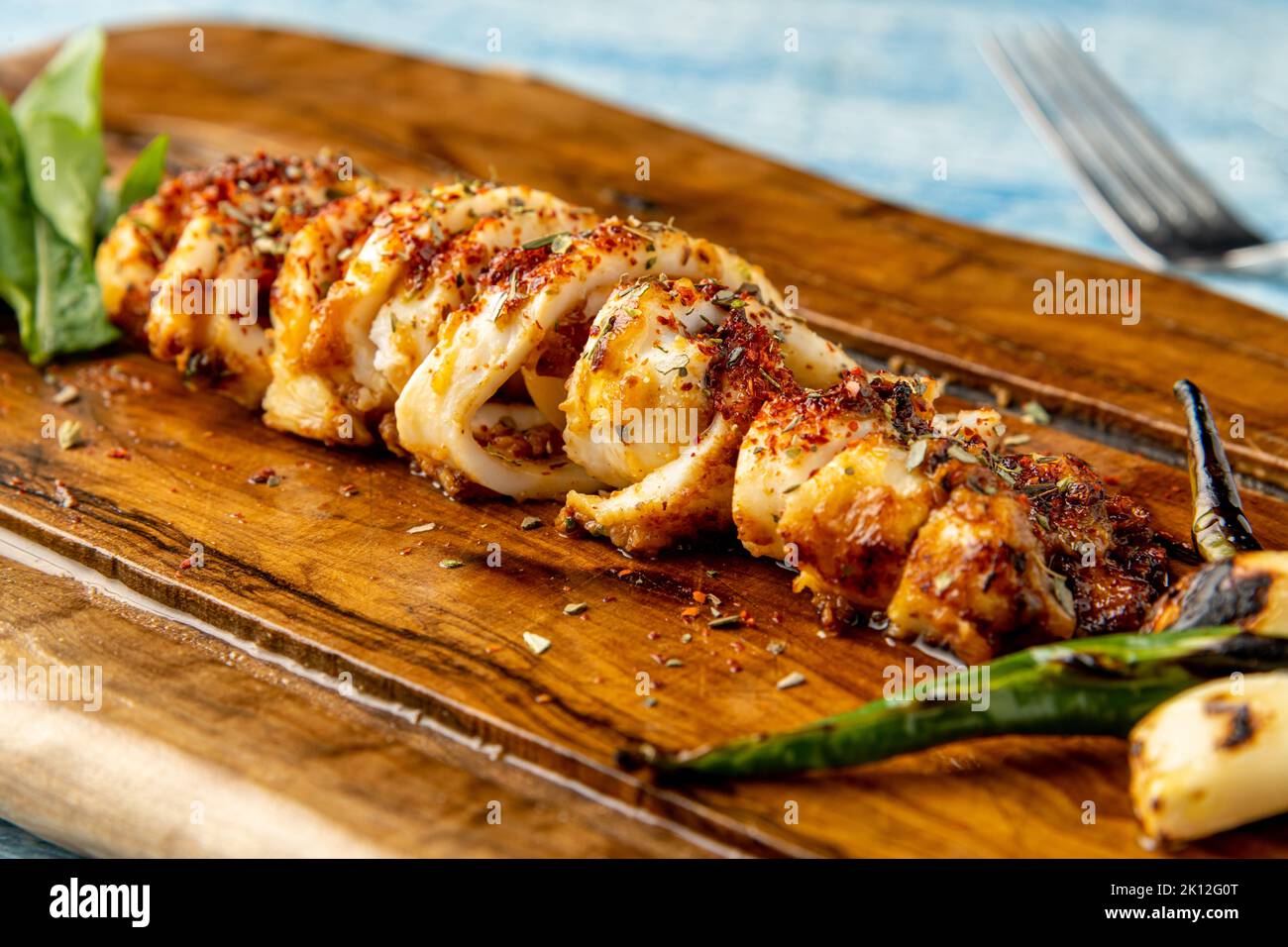 Spicy sliced grilled squid with green pepper and garlic on a wooden serving board Stock Photo