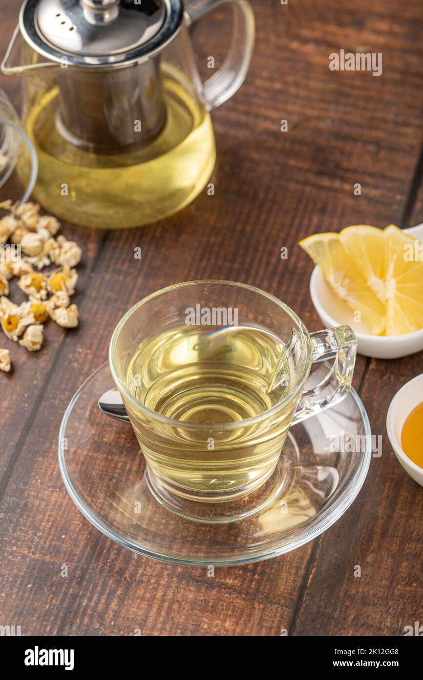 Relaxing chamomile tea in glass cup with lemon slices and honey next to it on wooden table. Stock Photo