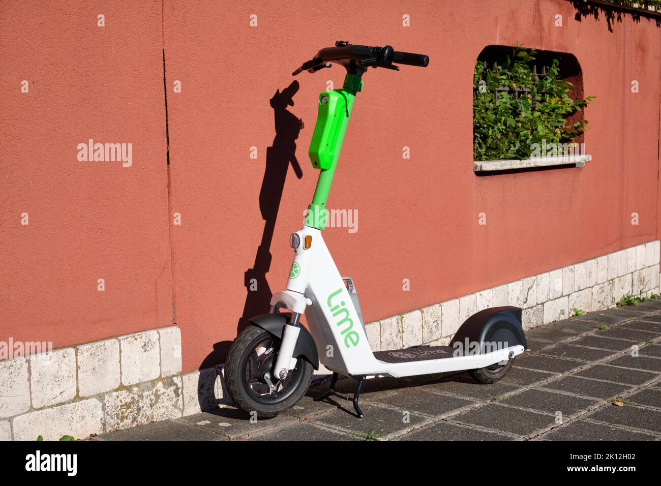 Nuremberg, Germany - August 23, 2022: An electric scooter of the company Lime is standing on the pavement in front of a red wall in the sunlight Stock Photo