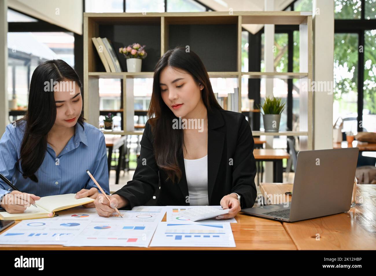 Two attractive young Asian businesswomen working and analyzing business financial data on the report together. Stock Photo