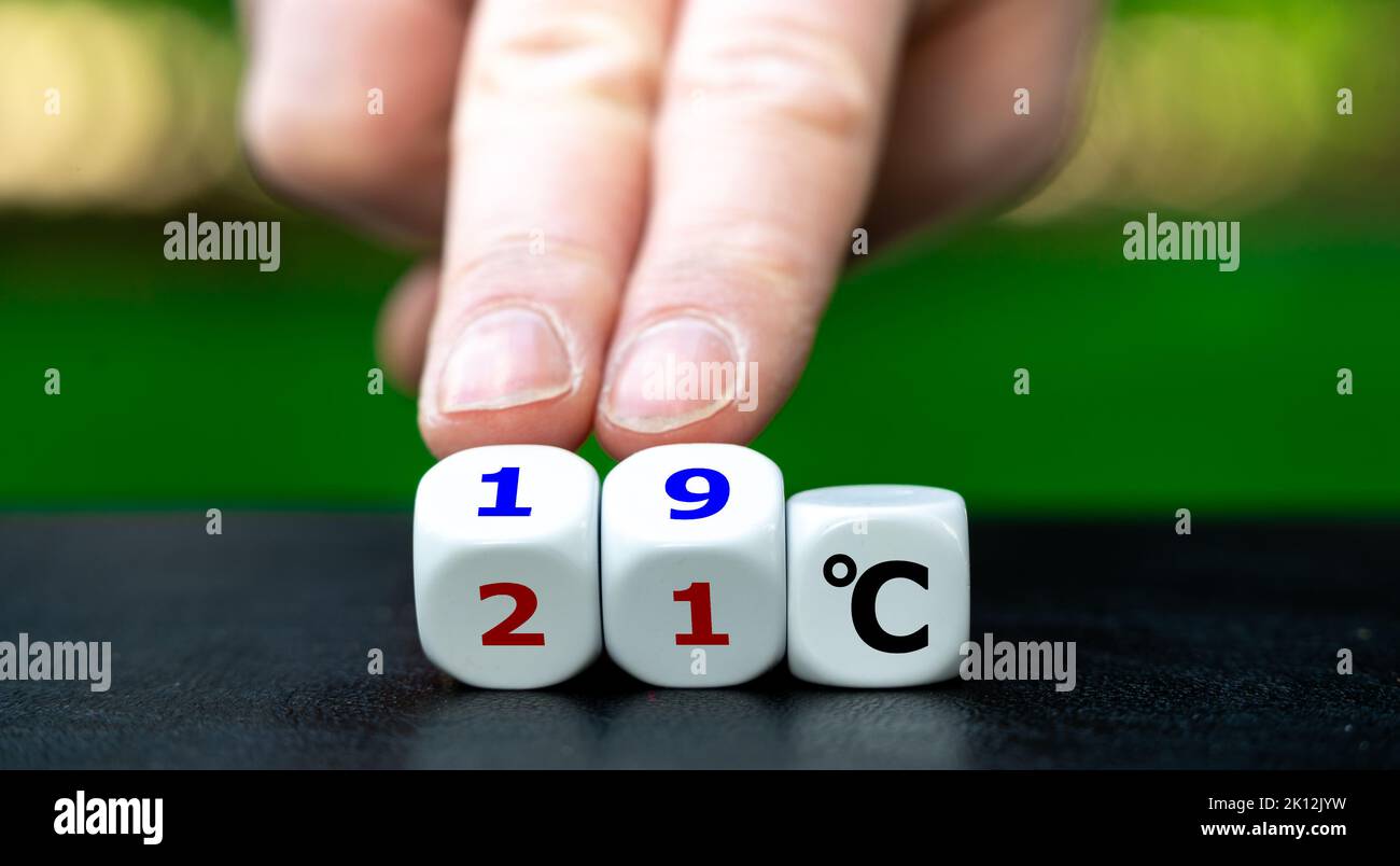 Hand turns dice and changes the expression '21 degrees Celsius' to '19 degrees Celsius'. Symbol for lowering the temperature in offices to reduce the Stock Photo
