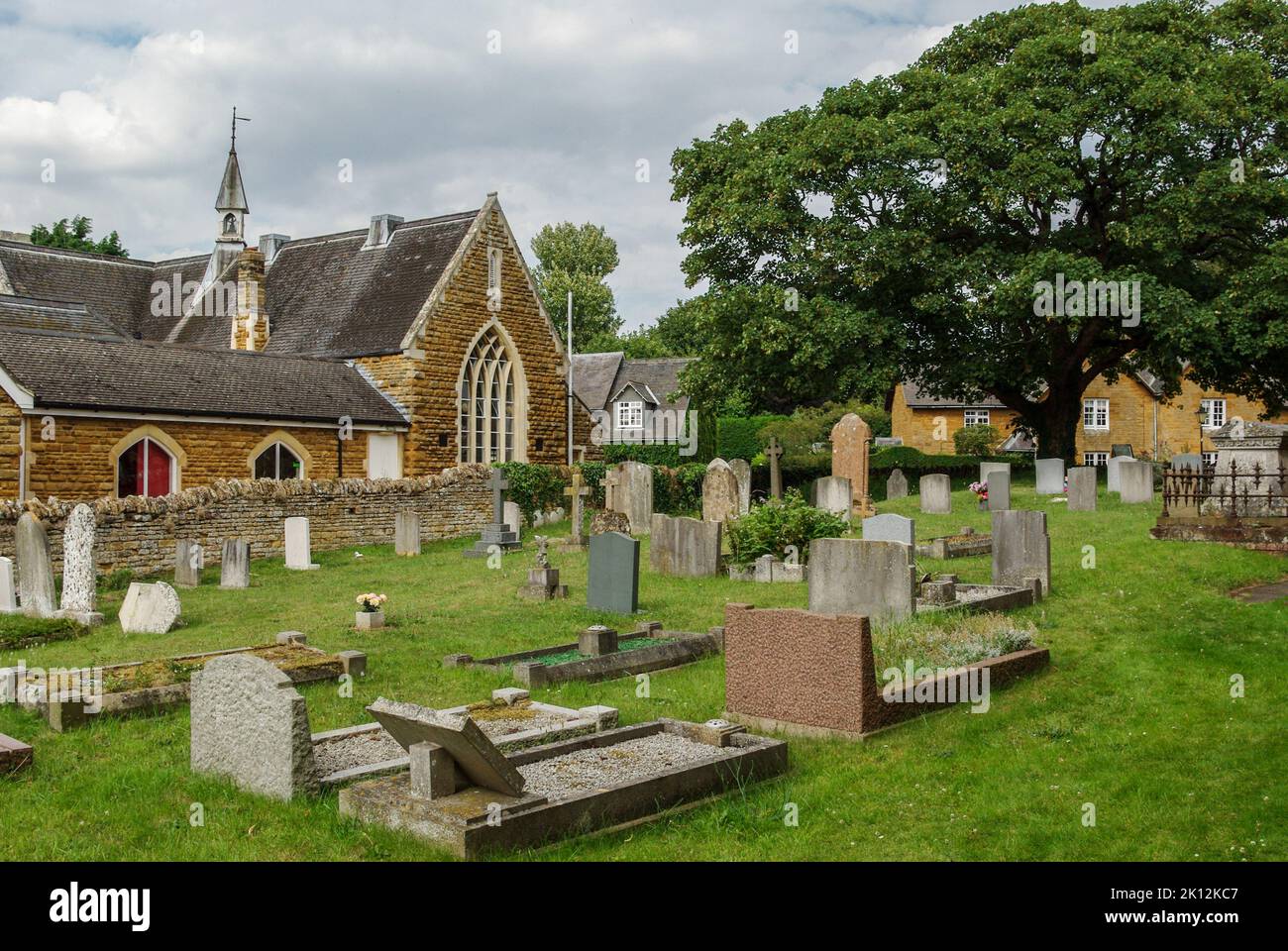 A view of the churchyard of St Peter and St Paul in the village of Sywell, Northamptonshire, UK; the Village Hall in the background Stock Photo