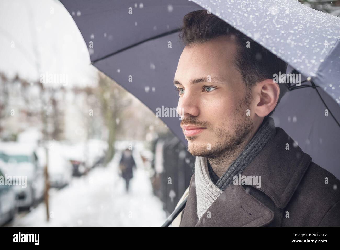 Portrait of a thoughtful young man with umbrella on London street in winter snow Stock Photo
