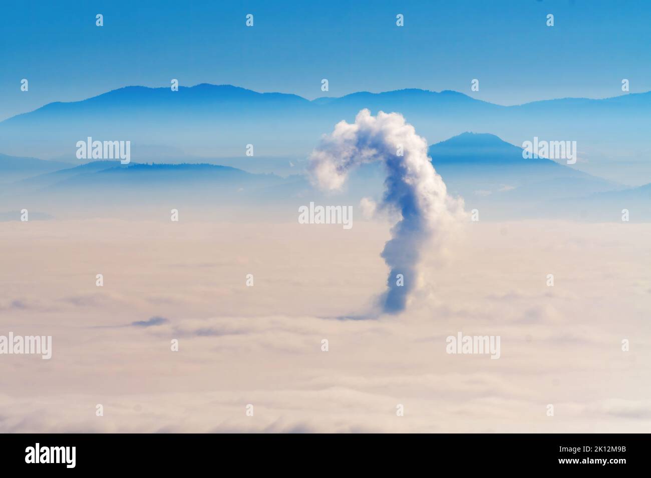 Foggy landscape with single plume of smoke from chimney above the city, hills visible in background. Environment, climate change and energy concepts Stock Photo