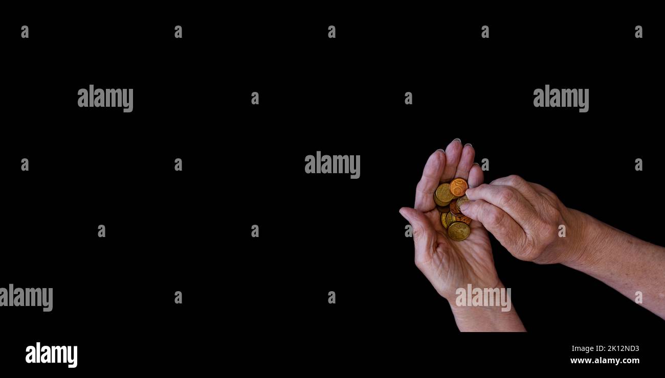 Black background with the hands of an elderly woman who holds coins ...