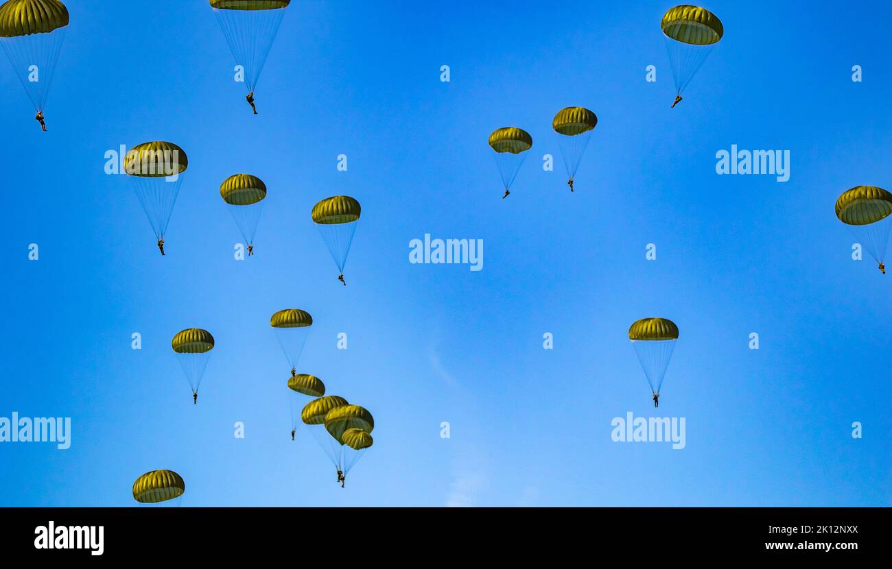 Military parachutist paratroopers parachute jumping out of a air force planes on a clear blue sky day with the moon. Stock Photo
