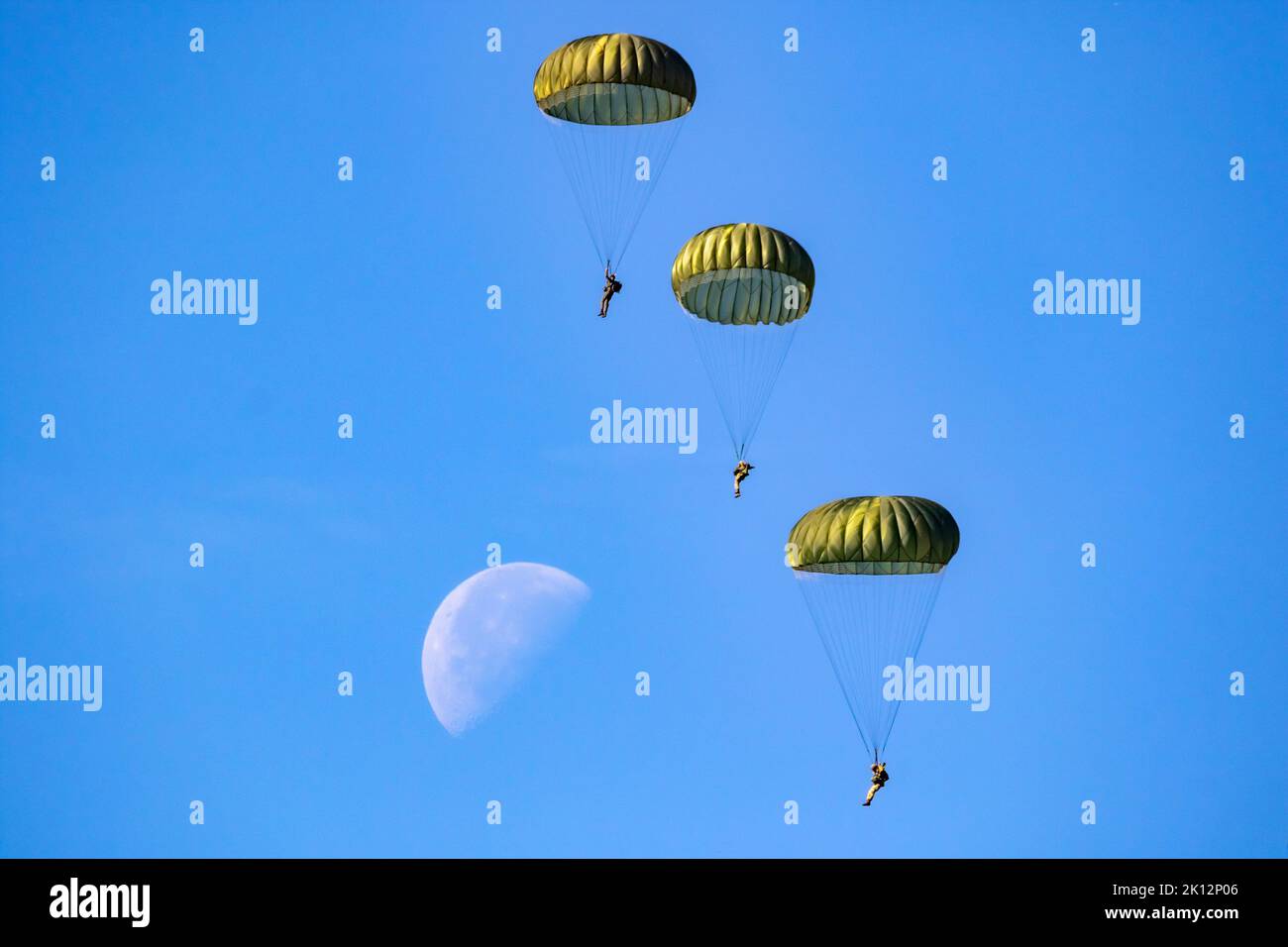 Military parachutist paratroopers parachute jumping out of a air force planes on a clear blue sky day with the moon. Stock Photo