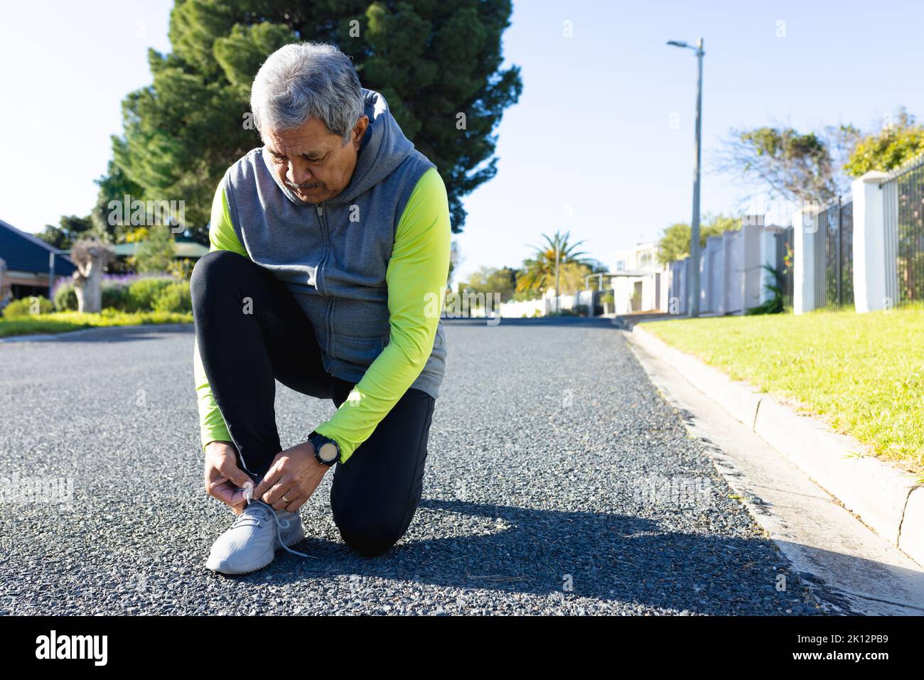 Senior biracial man in sports clothes kneeling in road tying shoelace