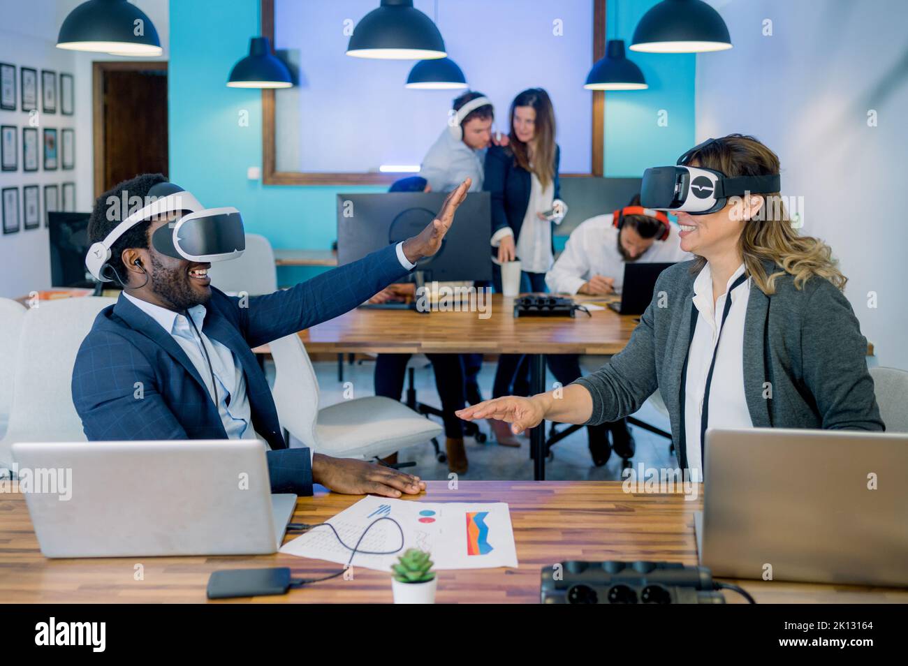 Cheerful multiethnic colleagues gesturing while exploring cyberspace in VR glasses in office Stock Photo
