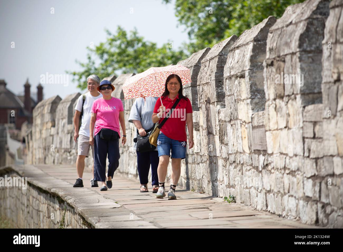 A woman on York’s city wall uses an unbrella to protect herself from the sun as people in the city of York, North Yorkshire endure the hottest day on Stock Photo