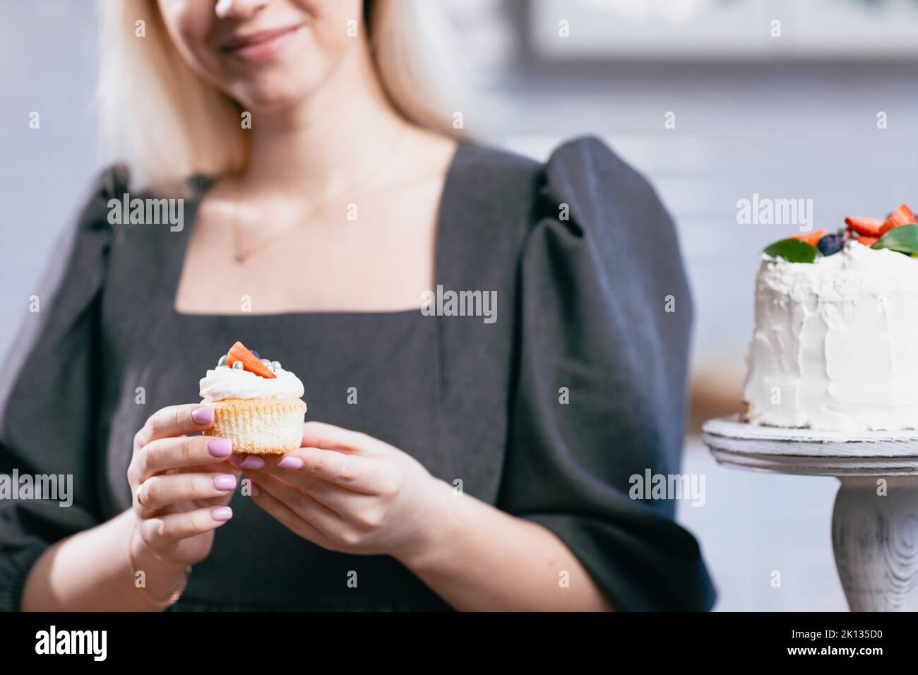 Pastry chef confectioner young caucasian woman holds cupcake in hands cake on kitchen table. Cakes cupcakes and sweet dessert Stock Photo