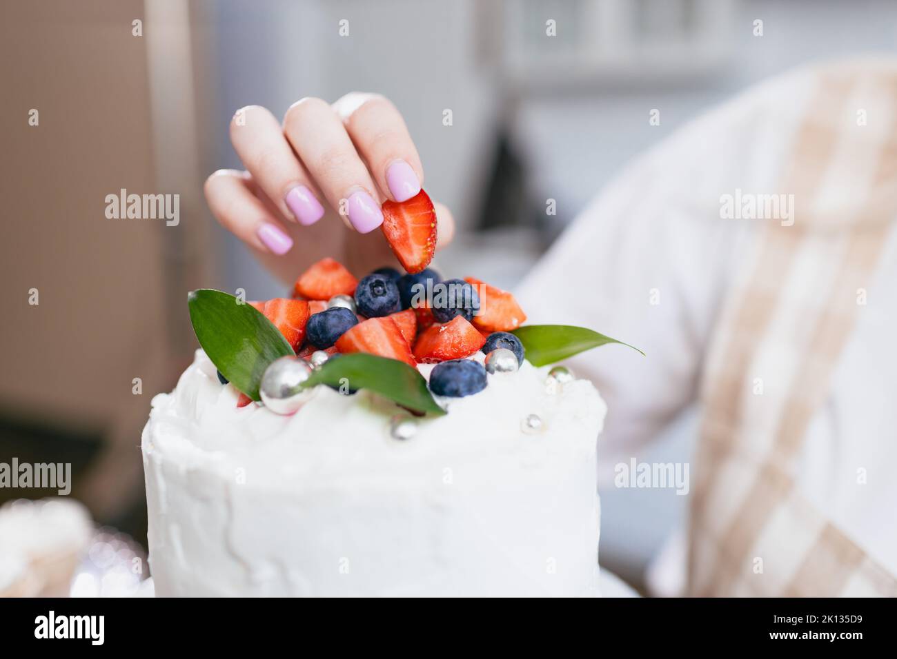 Pastry chef confectioner young caucasian woman decorate cake on kitchen table. Cakes cupcakes and sweet dessert Stock Photo