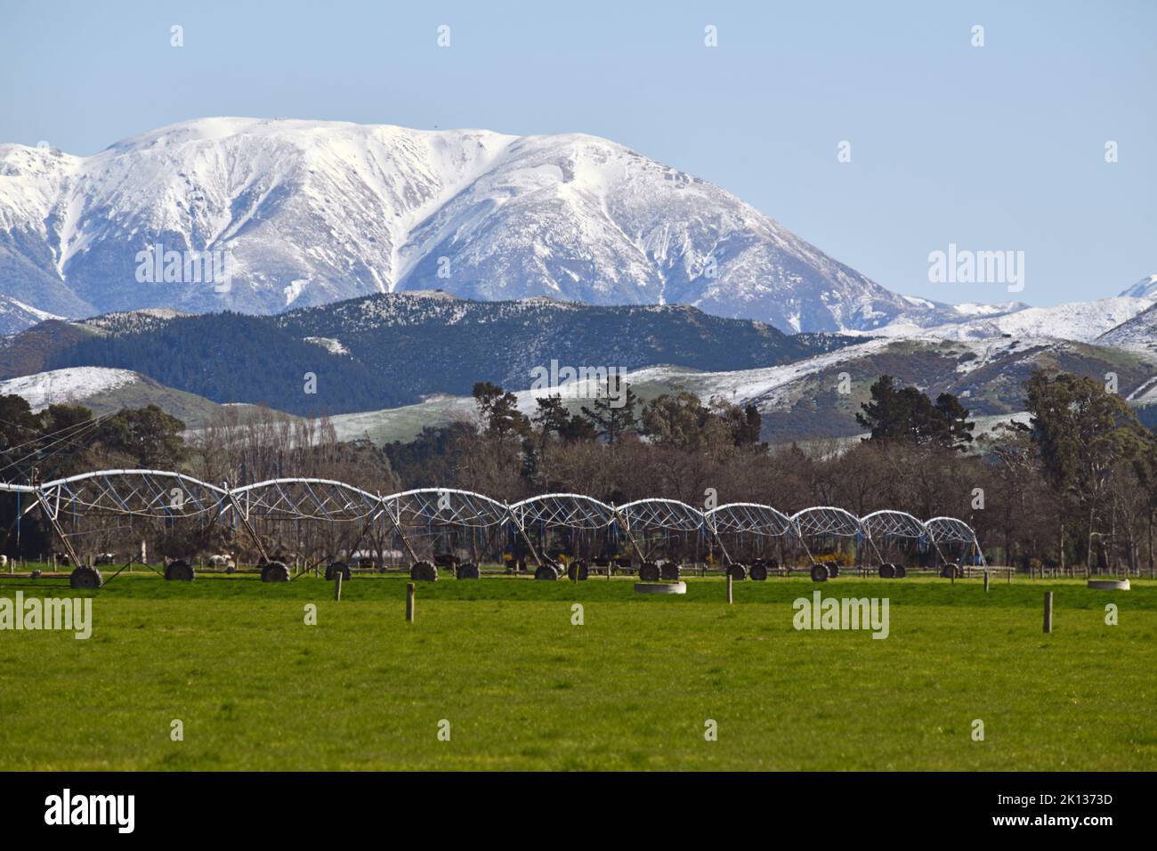 Iconic landscape in Canterbury, New Zealand, featuring a farm with irrigation gear and the Torlesse Range sprinkled with a rare spring snowfall in the Stock Photo