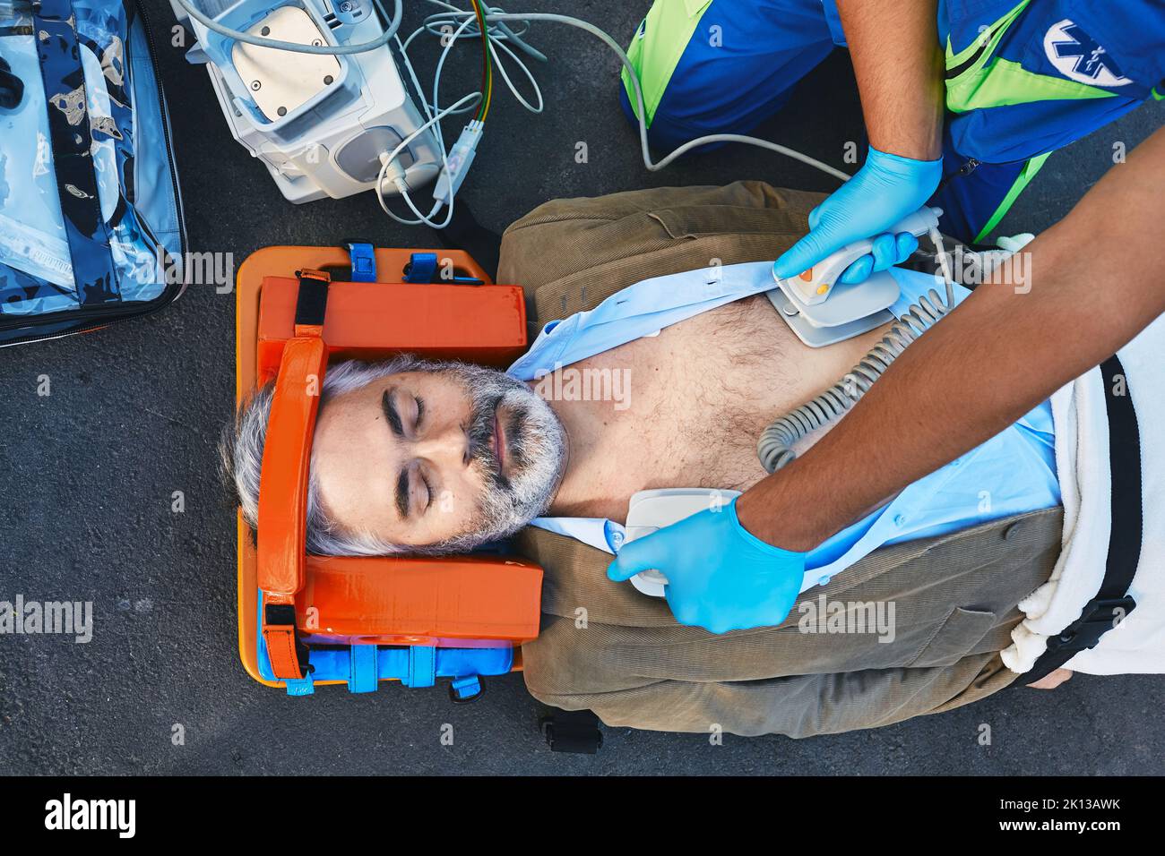 Ambulance paramedic using defibrillator performing cardiopulmonary resuscitation on casualty. First aid for injured mature man lying on emergency stre Stock Photo