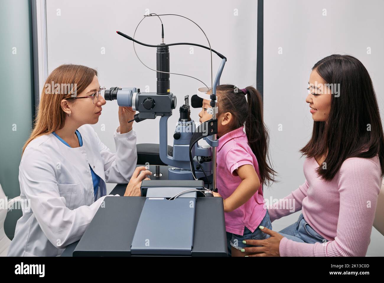 Japanese mother with her daughter while visit to optometrist. Little female child getting vision testing and eye exam in ophthalmology clinic, side vi Stock Photo