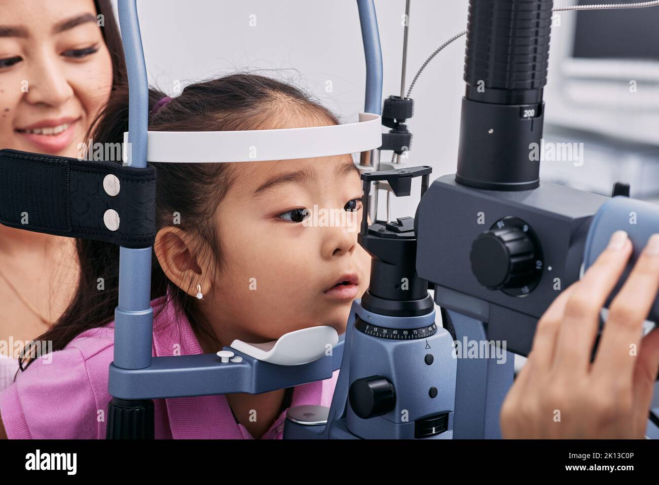Checking little Korean girl's eyesight with binocular slit lamp in ophthalmology clinic, close-up. Vision correction in children Stock Photo