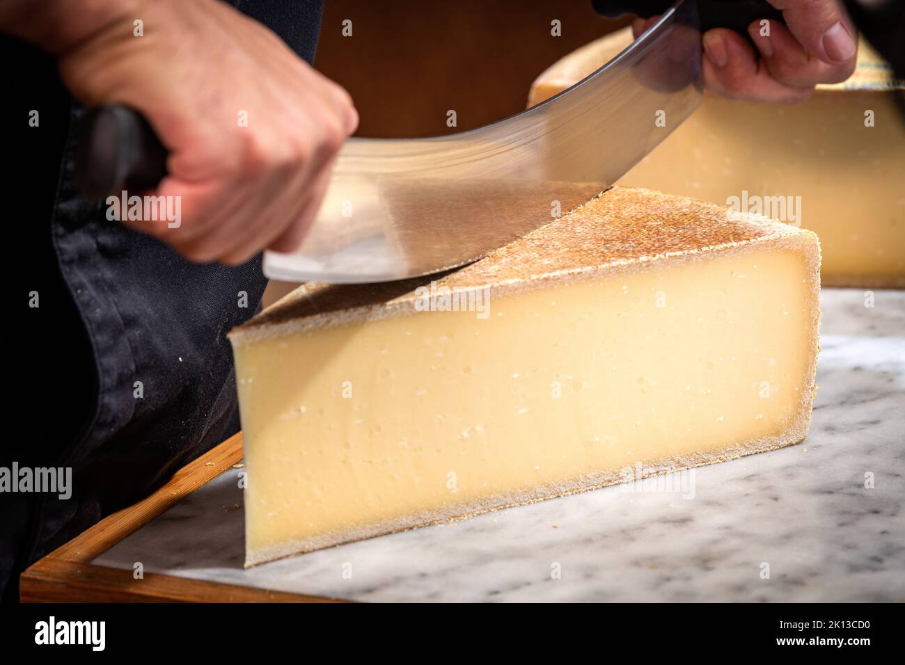 A man cuts a portion of The Gruyère with a wire, the famous swiss cheese in a cellar on a marbble background Stock Photo