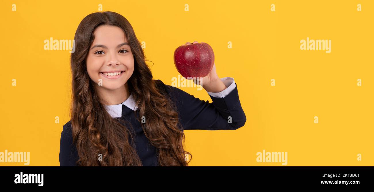 happy teen girl showing red vitamin apple for lunch on yellow background, vitamin. Child girl portrait with apple, horizontal poster. Banner header Stock Photo