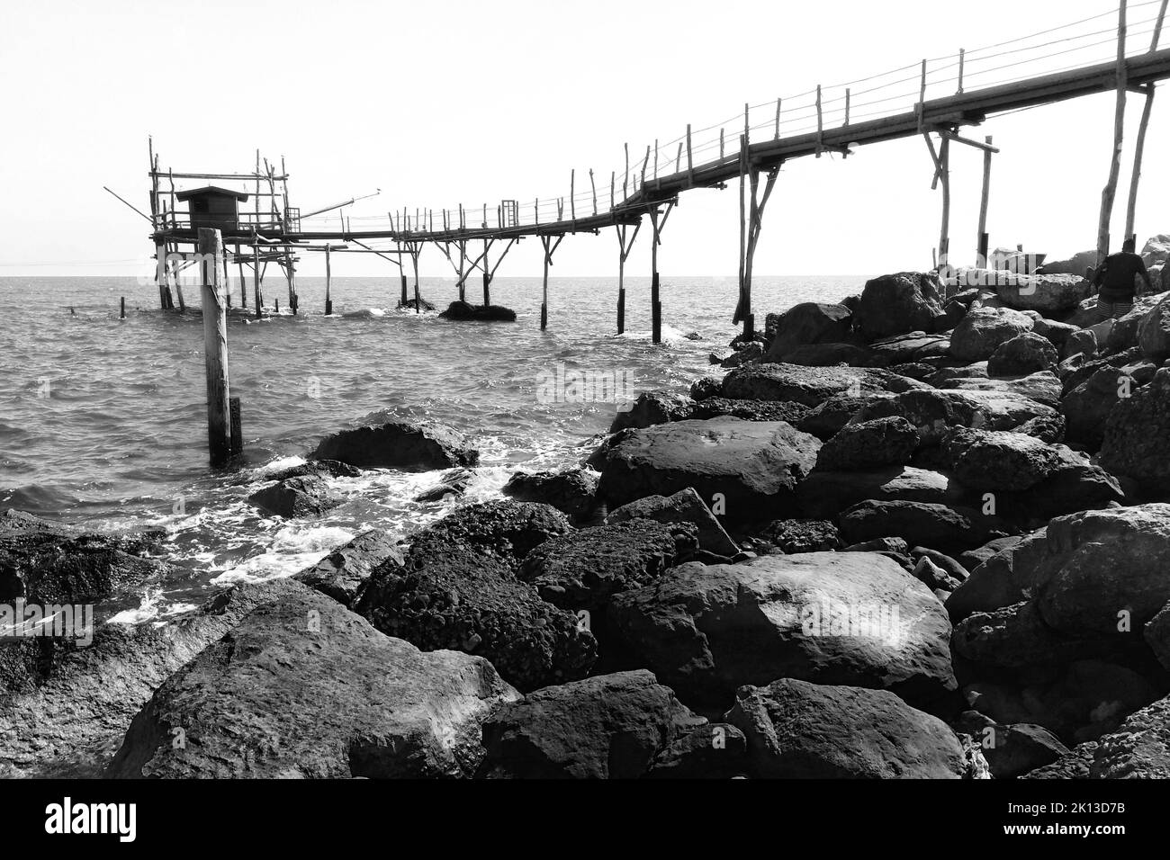 A grayscale of a rocky coast with an old wooden pier Stock Photo